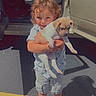 Waylon is registered to the contest to win money with this photo: child, puppy, dog, vehicle, parking_lot, yellow_line, curly_hair, shorts, sneakers, sunlight, shadow, holding, cute, outdoor, summer, smiling, young, pet, car_door, casual_clothing
