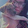 person, puppy, dog, glasses, hand, face, outdoor, blue_sky, floral_clothing, bracelet, young_adult, pet, closeup, holding, cute, expression, sunlight, portrait, animal, daytime