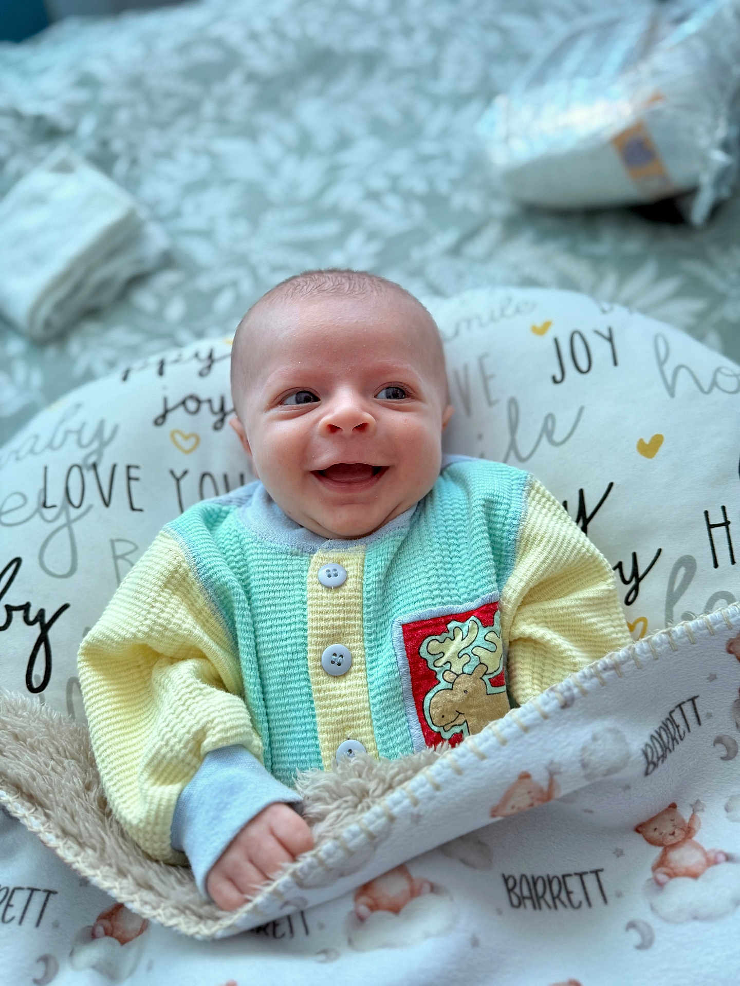 Barrett is registered to the contest to win money with this photo: baby, smile, blanket, cushion, clothing, infant, happy, face, hand, pattern, bed, soft, cozy, pastel_colors, indoor, portrait, cute, child, newborn, warm
