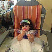 Sophia joined the competition — help win amazing prizes! chair, child, colorful, curly_hair, cushion, cute, dress, floor, flower_headband, furniture, girl, indoor, living_room, person, playful, purple, sitting, smile, toy, white