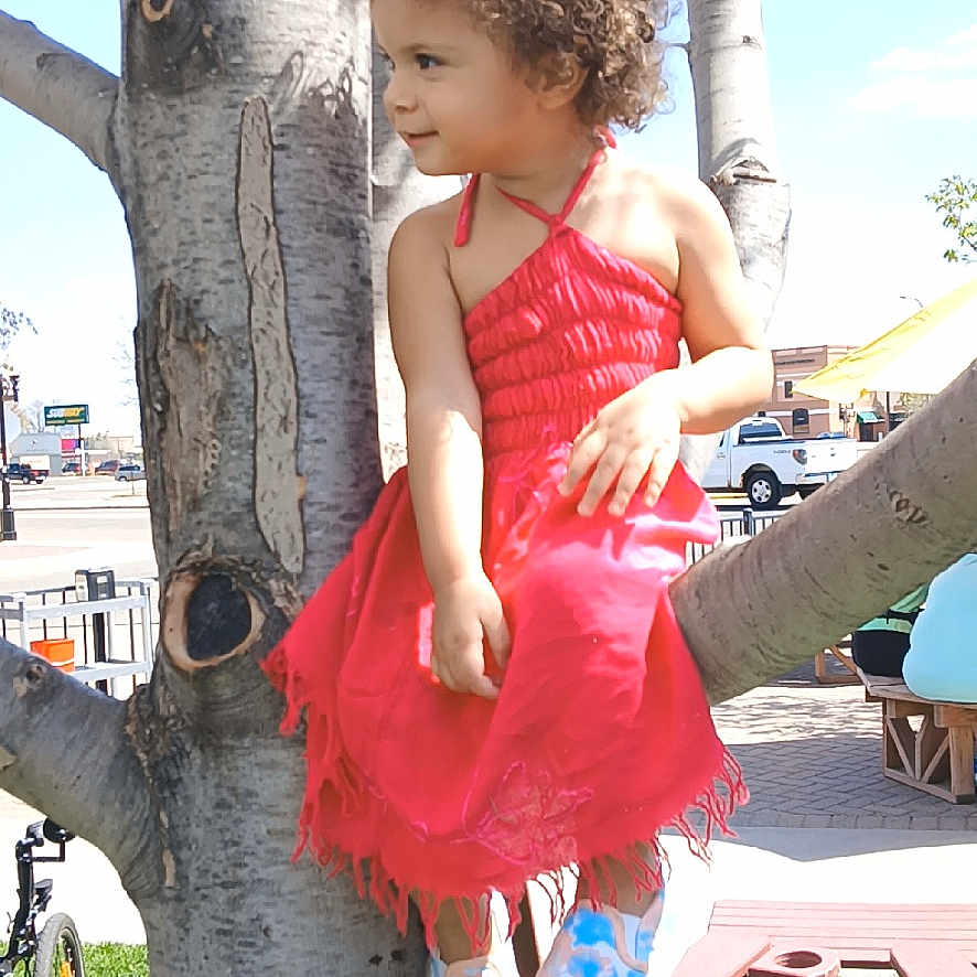 Ireland is registered to the contest to win money with this photo: bench, casual, child, clothing, curly_hair, daylight, grass, happy, nature, outdoor, park, person, playful, red_dress, shoes, smile, sunny, toddler, tree, urban