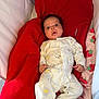 baby, infant, onesie, red_blanket, playpen, sleepwear, cute, surprised, lying_down, soft_fabric, indoor, child, newborn, face, expression, cozy, bedtime, patterned_clothing, comfort, resting