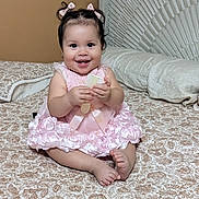 Ana Jazmin is registered to the contest to win money with this photo: baby, child, girl, pink_dress, smiling, sitting, bed, bedspread, patterned, hair_bows, indoor, headboard, happy, cute, infant, portrait, young_child, holding_object, cozy, home