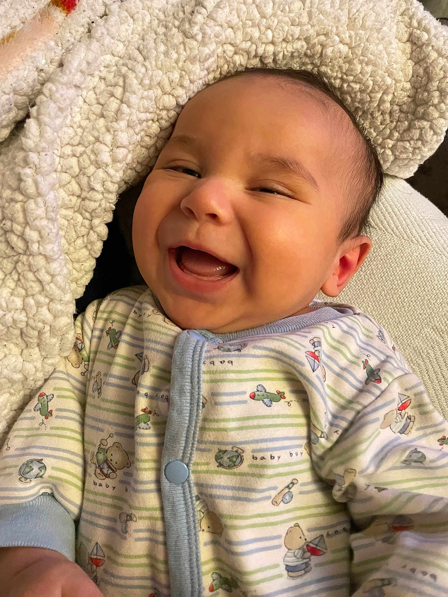 Silas is registered to the contest to win money with this photo: baby, infant, smiling, laughing, onesie, blanket, cozy, cute, child, happy, face, portrait, apparel, patterned_clothing, indoor, warm, soft_texture, closeup, person, newborn