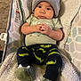 baby, infant, beanie, smiley_face, green_shirt, crocodile_pattern, pants, slippers, dinosaur_slippers, blanket, baby_seat, curious, hands_clasped, cute, indoor, portrait, child, young, cozy, soft_texture