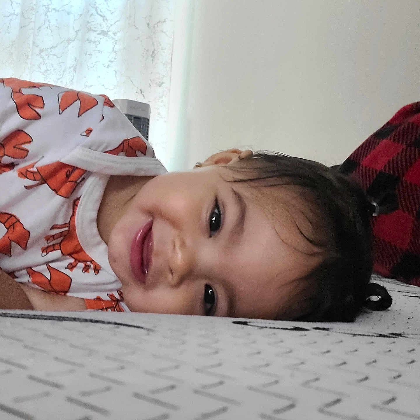 Breylin is registered to the contest to win money with this photo: bed, blanket, child, cozy, curtain, cute, face, hair, happy, home, indoor, lobster_pattern, orange, person, playful, resting, shirt, smiling, toddler, young