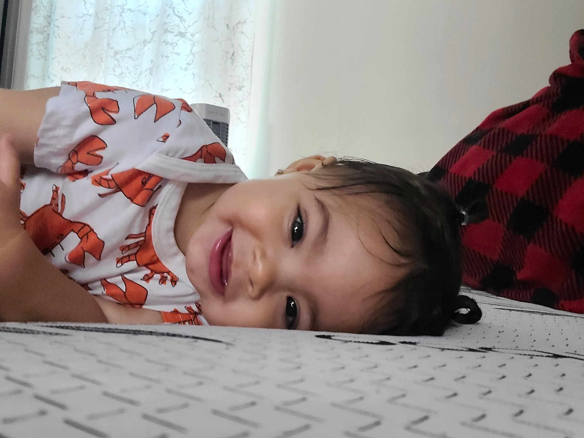Breylin is registered to the contest to win money with this photo: bed, blanket, child, cozy, curtain, cute, face, hair, happy, home, indoor, lobster_pattern, orange, person, playful, resting, shirt, smiling, toddler, young