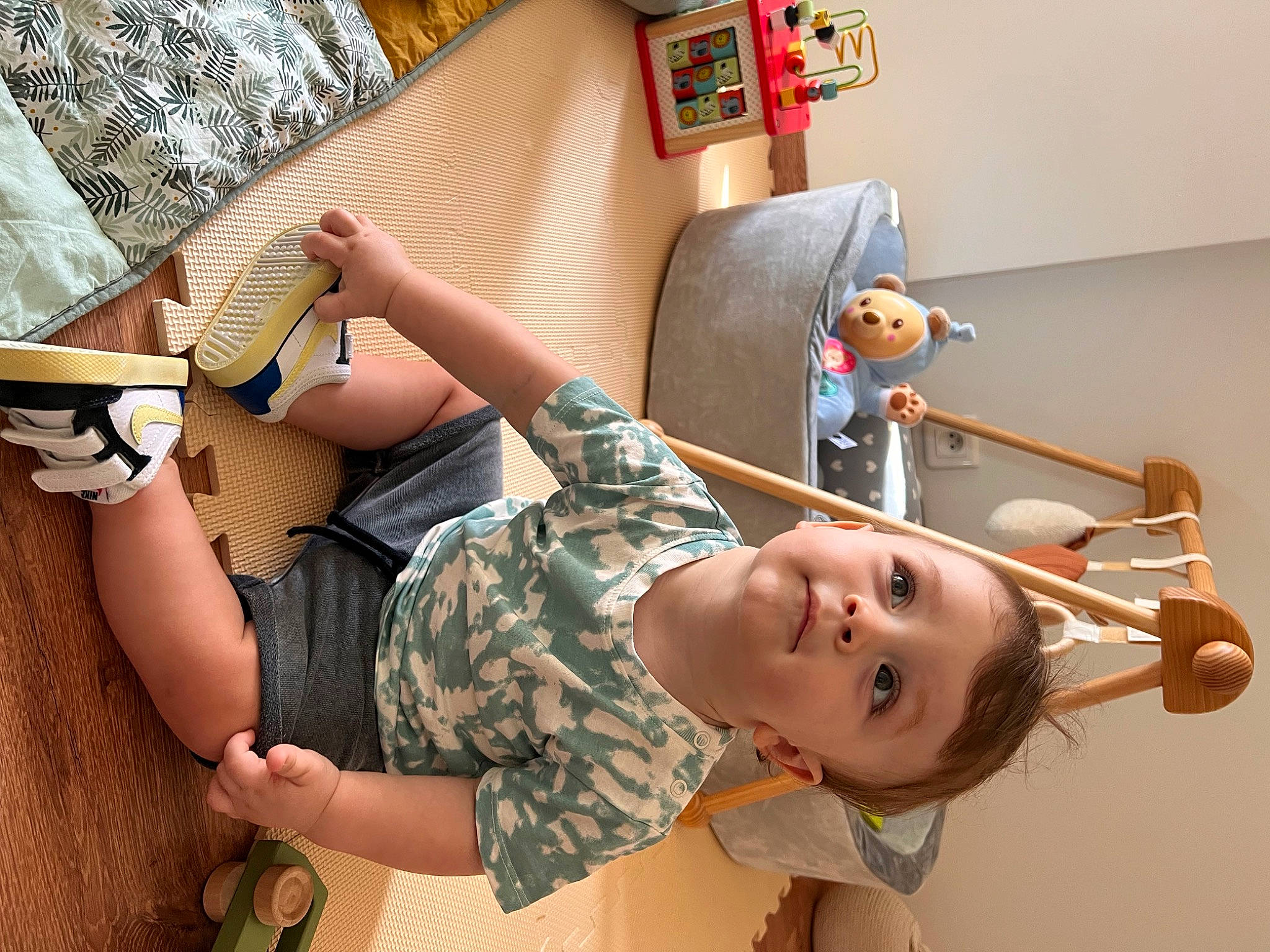 Ghjuvan participe au concours pour gagner de l'argent avec cette photo : arm, camouflage, child, eyewear, finger, fun, gesture, human_leg, knee, leisure, military_camouflage, person, play, room, sandal, shorts, sitting, smile, thigh, toddler