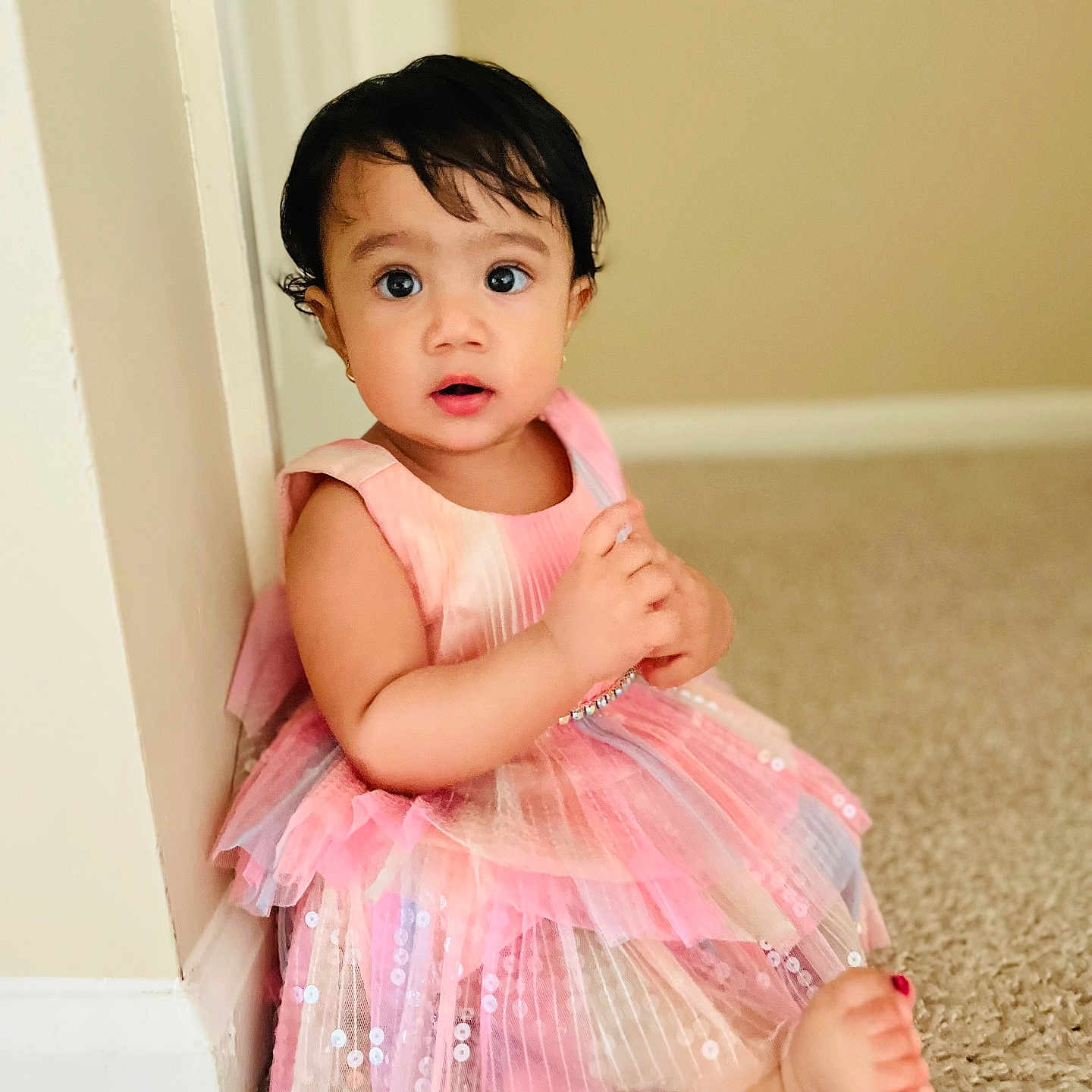 Nitya joined the competition — help win amazing prizes! barefoot, baseboard, carpet, casual, child, curly_hair, cute, expression, indoor, innocence, pink_dress, portrait, sitting, skin, small_earrings, soft_lighting, toddler, wall, wide_eyes, young_child