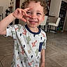 Zaylin is registered to the contest to win money with this photo: child, boy, smiling, curly_hair, cactus_shirt, hand_gesture, indoor, living_room, tile_floor, furniture, chair, cabinet, modern, happy, portrait, casual_clothing, playful, young, person, home