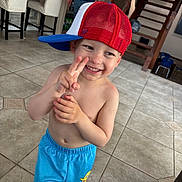 Zaylin is registered to the contest to win money with this photo: child, toddler, smile, cap, red_cap, blue_cap, barefoot, tile_floor, indoor, home, staircase, bar_stools, shorts, blue_shorts, peace_sign, happy, playful, person, casual, cute
