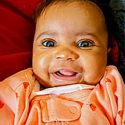 Alexi is registered to the contest to win money with this photo: baby, smiling, infant, face, eyes, clothing, ladybug_pattern, orange_outfit, portrait, happy, cute, lying_down, red_blanket, gray_blanket, closeup, child, newborn, human, indoors, cozy