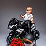 baby, child, motorcycle, toy, leather_jacket, leather_pants, helmet, roses, bouquet, white_tshirt, black, studio, portrait, pose, floor, wheel, handlebar, expression, indoor, background