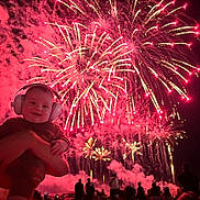 Malone participe au concours pour gagner de l'argent avec cette photo : baby, headphones, fireworks, night, celebration, crowd, silhouette, person, smile, holding, outdoor, festive, event, colorful, bright, sky, happy, fun, party, light