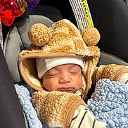 Carlos is registered to the contest to win money with this photo: baby, sleeping, car_seat, blanket, toy, hood, pom_poms, clothing, warm, infant, striped, mittens, soft, cute, child, face, headwear, cozy, indoors, resting