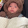 baby, child, infant, car_seat, bear_hoodie, blanket, fur_clothing, cute, wide_eyes, portrait, warm_clothing, indoors, seatbelt, expression, face, young_child, cozy, soft_texture, warning_sign, closeup