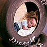baby, tire, blanket, infant, clothing, jeans, white_shirt, face, head, lying_down, soft_texture, curious_expression, outdoor, closeup, portrait, child, cushion, resting, round_shape, hoosier