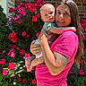baby, brick_wall, bright_colors, child, flowers, garden, greenery, happy, holding, nature, outdoor, person, pink_shirt, portrait, roses, smile, sunlight, tattoo, tongue_out, woman