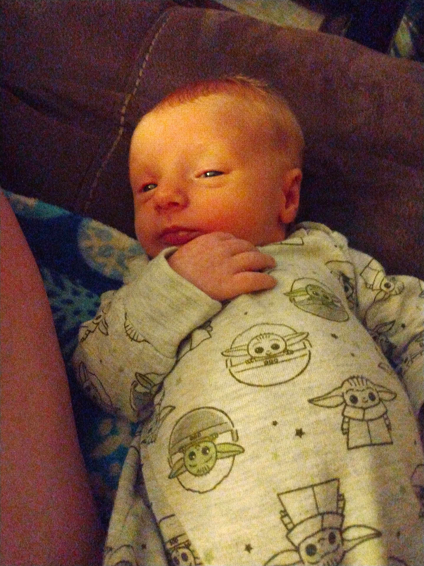 Jesson joined the competition — help win amazing prizes! baby, infant, onesie, baby_yoda, star_wars, couch, hand, face, sleepy, curious, clothing, child, young, indoors, portrait, person, cute, soft_lighting, home, relaxed