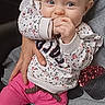 baby, child, person, blue_eyes, light_hair, pink_pants, floral_sweater, hand, face, adult_hand, gray_hoodie, red_glitter_heart, indoor, seated, cute, playful, curious, portrait, clothing, holding