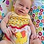 Giovanna is registered to the contest to win money with this photo: baby, child, smiling, yellow_clothing, patterned_clothing, baby_seat, elephant_design, colorful, happy, indoors, cute, toddler, infant, face, hand, legs, hair, seat, toy, playful