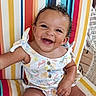 Aria is registered to the contest to win money with this photo: baby, child, infant, smiling, happy, portrait, curly_hair, earrings, seated, chair, striped_background, colorful, outdoor, wicker_furniture, romper, tropical_pattern, close_up, joyful, photography, sunlight