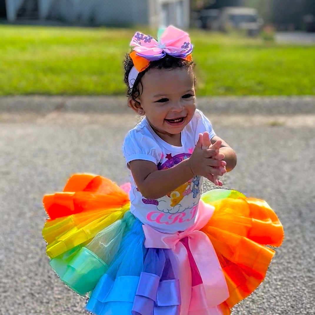 Aria joined the competition — help win amazing prizes! child, toddler, smiling, clapping, rainbow_tutu, colorful_dress, hair_bow, outdoor, sunlight, driveway, house, lawn, portrait, full_body, fashion, happy, shoes, curly_hair, residential_area, celebration