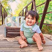 Matthyus is registered to the contest to win money with this photo: baby, bridge, child, cute, daylight, face, greenery, happy, infant, nature, one, outdoor, person, portrait, romper, sitting, smiling, sunlight, wood, wooden_floor