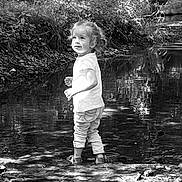 Juliette a rejoint le concours — aidez-le/la à gagner de superbes lots ! child, toddler, water, creek, nature, outdoor, reflection, plants, trees, rocks, shoes, pants, shirt, black_and_white, curly_hair, smile, standing, daylight, forest, playful