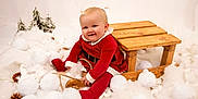 Darcie-Rose joined the competition — help win amazing prizes! baby, child, red_clothing, wooden_sled, snow_balls, fluffy, pine_trees, winter_theme, festive, smiling, indoors, cute, holiday, playful, portrait, white_background, soft_texture, seasonal, happy, sitting