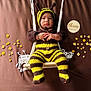 Dylan is registered to the contest to win money with this photo: baby, bee, black, brown_background, child, costume, cute, decorations, feet, flowers, hands, infant, knitwear, plaque, portrait, striped, swing, three_months, wooden, yellow