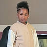 afro_hairstyle, braids, child, collar, confidence, earrings, fashion, girl, home_interior, indoors, jacket, looking_at_camera, neutral_background, person, portrait, serious_expression, standing, upper_body, wall, young_person