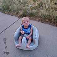 Koda is registered to the contest to win money with this photo: baby, child, outdoor, seat, plastic_seat, sidewalk, grass, plants, concrete, blue_clothing, infant, person, sitting, footwearless, nature, summer, young_child, casual, expression, sunlight