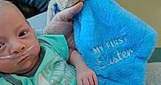 Koda is registered to the contest to win money with this photo: baby, infant, nasal_tube, plush_toy, blue_blanket, green_onesie, hand, person, jeans, hospital, medical_care, cute, soft_toy, child, newborn, sitting, comfort, tenderness, indoor, holding