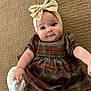 Lilah is registered to the contest to win money with this photo: baby, infant, child, headband, bow, plaid_dress, carpet, texture, cute, smiling, happy, indoors, portrait, person, clothing, footwear, white_sock, hand, face, eyes