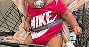 Layla is registered to the contest to win money with this photo: baby, infant, child, shopping_cart, supermarket, pink_bow, pacifier, nike_shirt, blanket, sitting, portrait, face, eyes, smiling, clothing, socks, grocery_store, metal_cart, indoor, shopping