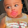 Layla is registered to the contest to win money with this photo: baby, infant, child, portrait, face, eyes, pacifier, smiling, indoor, close_up, sitting, clothing, outfit, yellow_shirt, pink_pacifier, blue_lights, home, background, photography, cute
