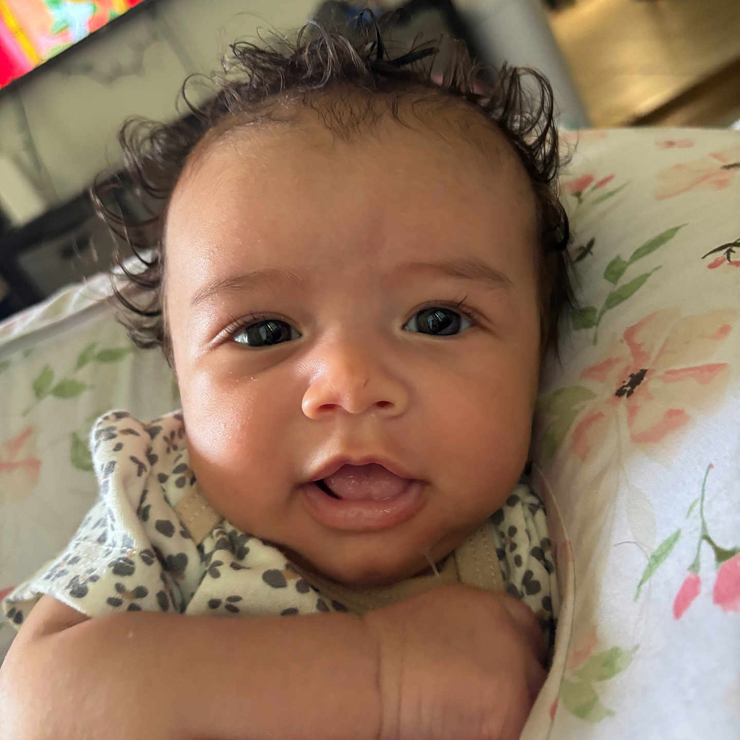 Maeves is registered to the contest to win money with this photo: baby, blanket, child, closeup, clothing, curly_hair, cute, expression, eyes, face, floral_pattern, hand, indoors, infant, newborn, person, portrait, skin, smiling, young_child