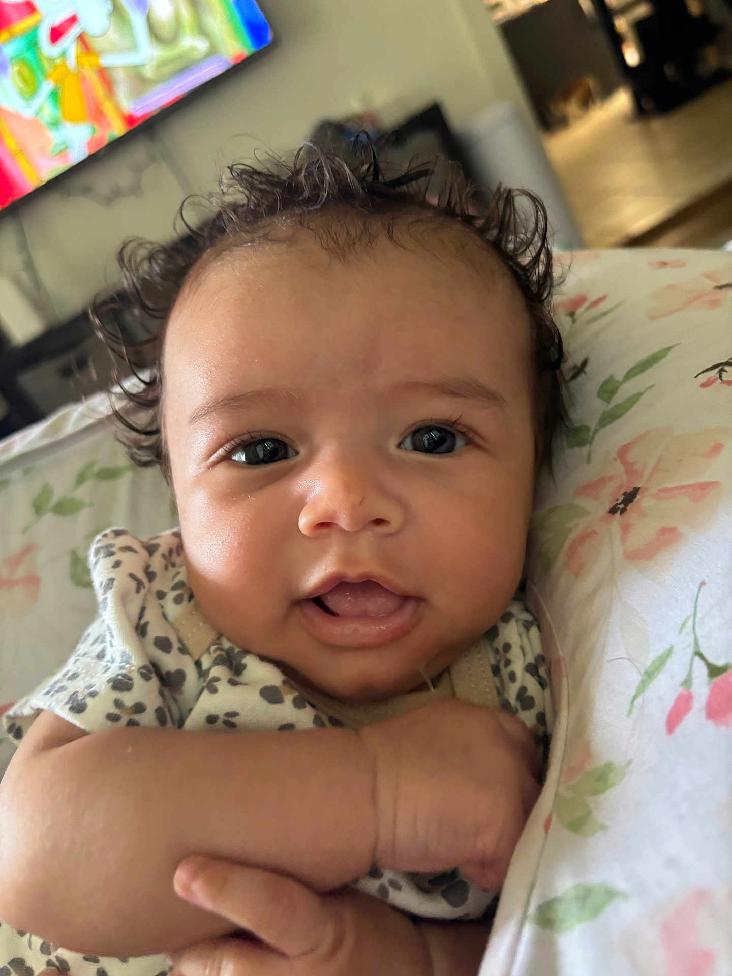 Maeves is registered to the contest to win money with this photo: baby, infant, face, curly_hair, eyes, expression, blanket, floral_pattern, hand, skin, portrait, indoors, cute, young_child, person, clothing, closeup, newborn, child, smiling