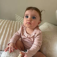 Charlotte is registered to the contest to win money with this photo: baby, child, infant, blue_eyes, pink_clothing, long_sleeves, curly_hair, sitting, blanket, plush, soft_texture, indoor, cozy, cute, portrait, young_child, curious, natural_light, face, hands