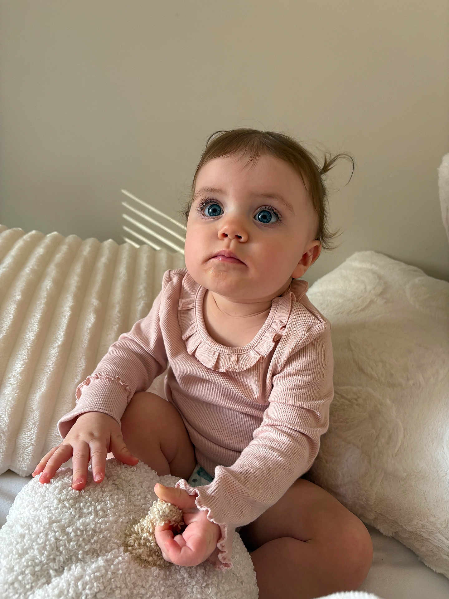 Charlotte is registered to the contest to win money with this photo: baby, child, infant, blue_eyes, pink_clothing, long_sleeves, curly_hair, sitting, blanket, plush, soft_texture, indoor, cozy, cute, portrait, young_child, curious, natural_light, face, hands