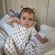 Lottie is registered to the contest to win money with this photo: toddler, child, bed, pigtails, dress, floral_pattern, plush_toy, white_bedspread, curious_expression, bracelet, blue_eyes, indoor, headboard, portrait, sitting, cute, young_child, soft_lighting, person, cozy