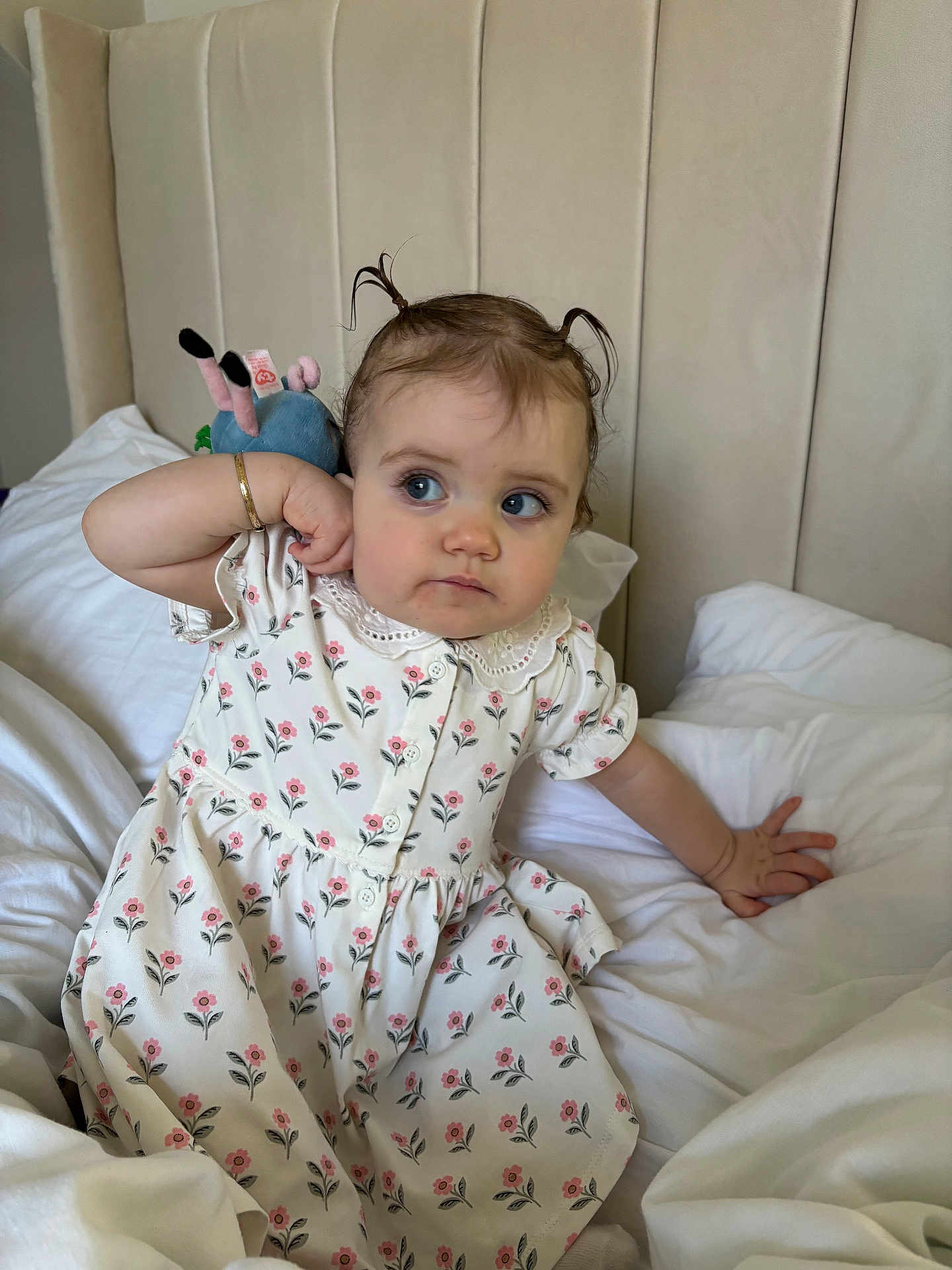 Lottie is registered to the contest to win money with this photo: toddler, child, bed, pigtails, dress, floral_pattern, plush_toy, white_bedspread, curious_expression, bracelet, blue_eyes, indoor, headboard, portrait, sitting, cute, young_child, soft_lighting, person, cozy