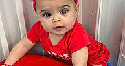 Vida is registered to the contest to win money with this photo: baby, infant, child, portrait, face, blue_eyes, wide_eyed, red_outfit, red_bow, headband, crawling, sitting, indoors, curtains, cushion, soft_furniture, colorful, close_up, smiling, photography