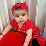 Vida is registered to the contest to win money with this photo: baby, infant, child, portrait, face, blue_eyes, wide_eyed, red_outfit, red_bow, headband, crawling, sitting, indoors, curtains, cushion, soft_furniture, colorful, close_up, smiling, photography