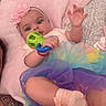 baby, child, infant, portrait, lying_down, pink_pillow, flower_headband, rainbow_dress, tulle_skirt, baby_toy, rattle, smiling, face, eyes, indoor, bed, blanket, colorful, pastel, photography
