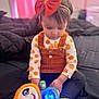 Mary is registered to the contest to win money with this photo: bed, black, blanket, bow, child, clothing, colorful, cute, focused, glowing_toy, headband, indoor, orange, pink, portrait, pumpkin_pattern, sitting, soft_lighting, toddler, toy