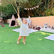 Giulia participe au concours pour gagner de l'argent avec cette photo : toddler, child, grass, outdoor, garden, teddy_bear, toy, blanket, play_area, smile, happy, sunlight, decorations, party_hat, tree, tent, cushion, barefoot, person, celebration