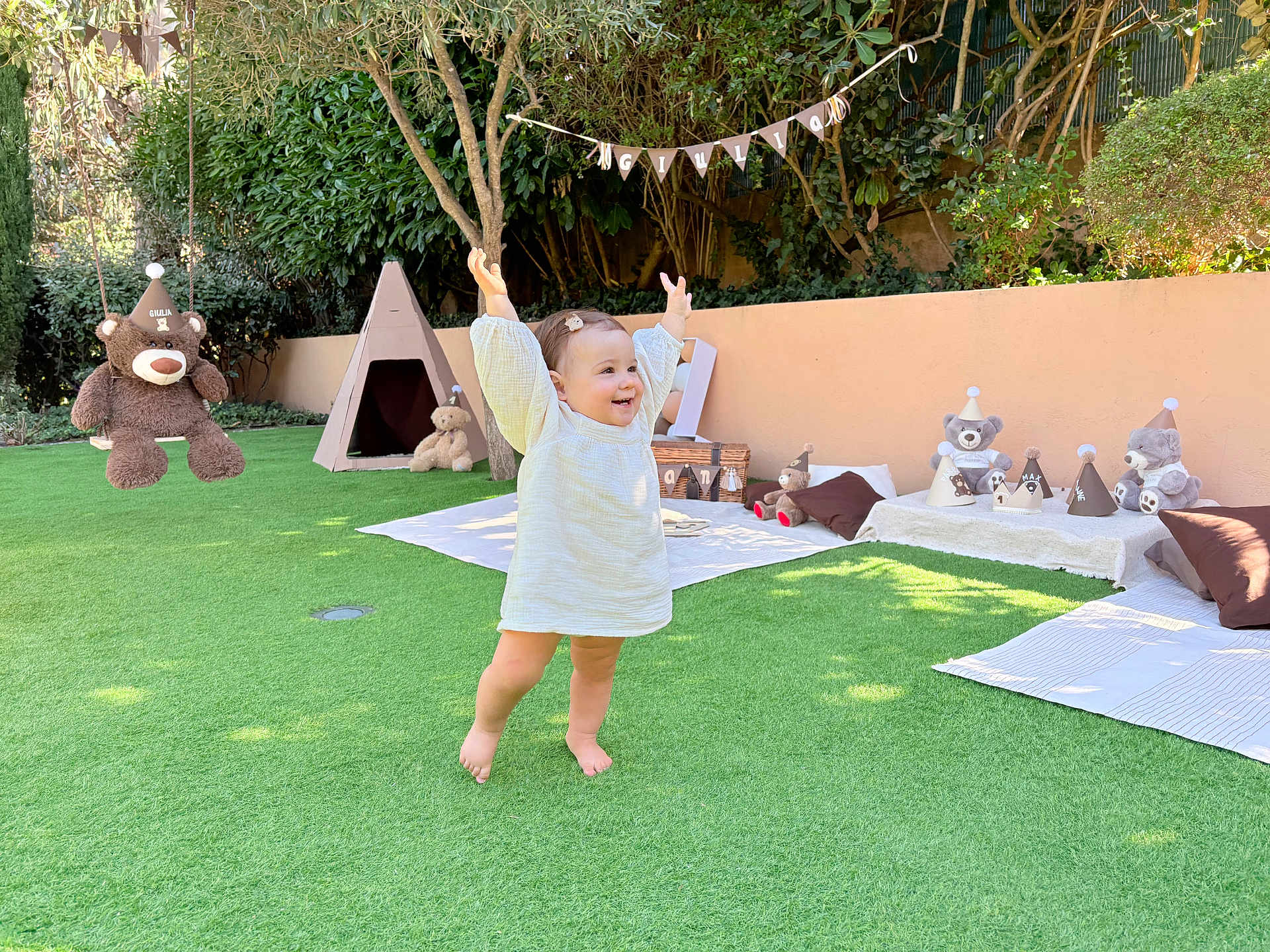 Giulia participe au concours pour gagner de l'argent avec cette photo : toddler, child, grass, outdoor, garden, teddy_bear, toy, blanket, play_area, smile, happy, sunlight, decorations, party_hat, tree, tent, cushion, barefoot, person, celebration