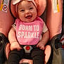 baby, smiling, car_seat, pink, headband, bib, clothing, infant, child, cute, happy, footwear, sitting, indoor, person, face, young_child, accessory, seat_belt, toy